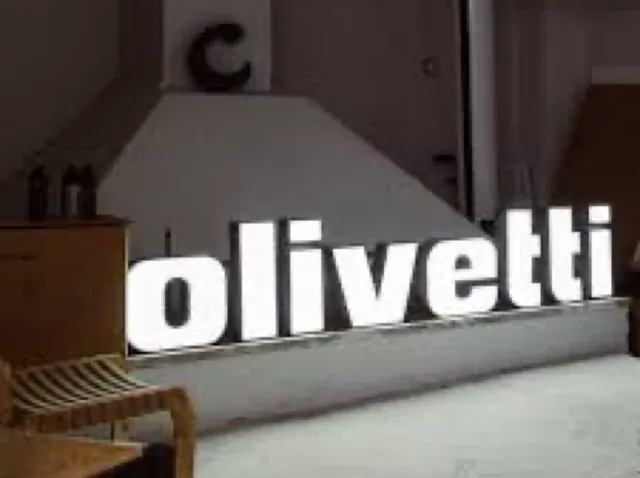 Insegna "olivetti" retroilluminata con sedia in legno in primo piano